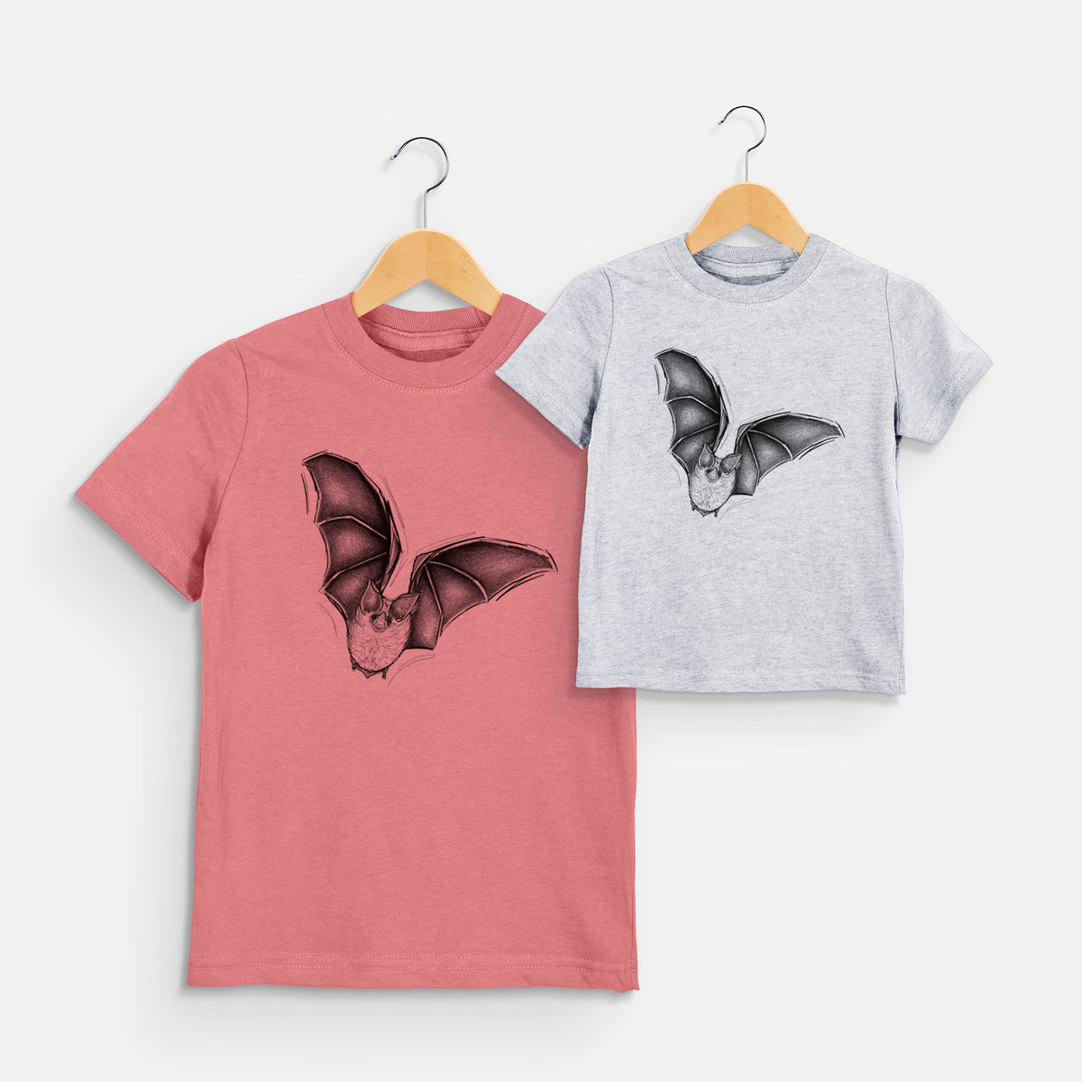 Two youth t-shirts in different colors on hangers, printed with a detailed black ink illustration of a California leaf-nosed bat in flight.