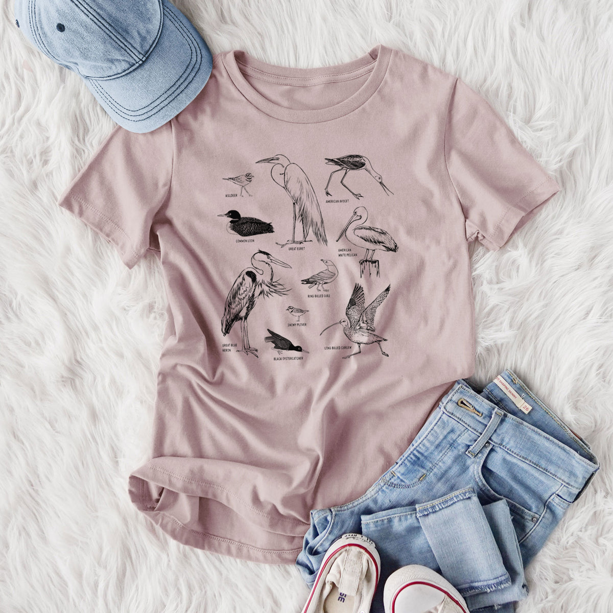 Women's relaxed fit cotton t-shirt printed with a chart of black ink California shorebirds, including herons, egrets, avocets and sandpipers, styled flat on a white faux fur rug with jeans.