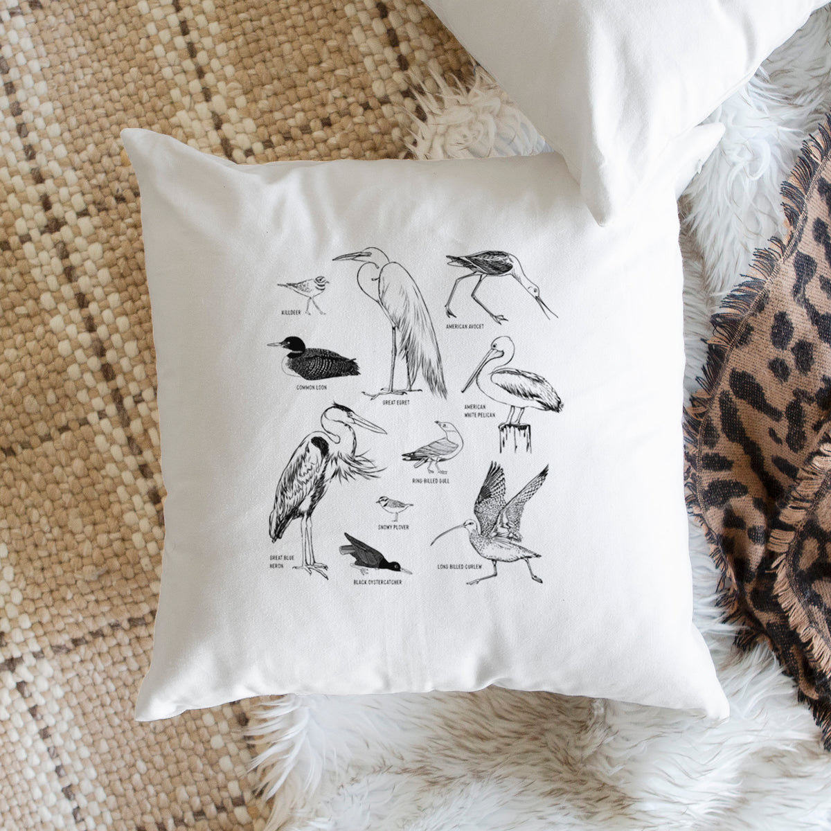 White pillow cover printed with a chart of black ink California shorebirds, including herons, egrets, avocets and sandpipers, on a woven chair.