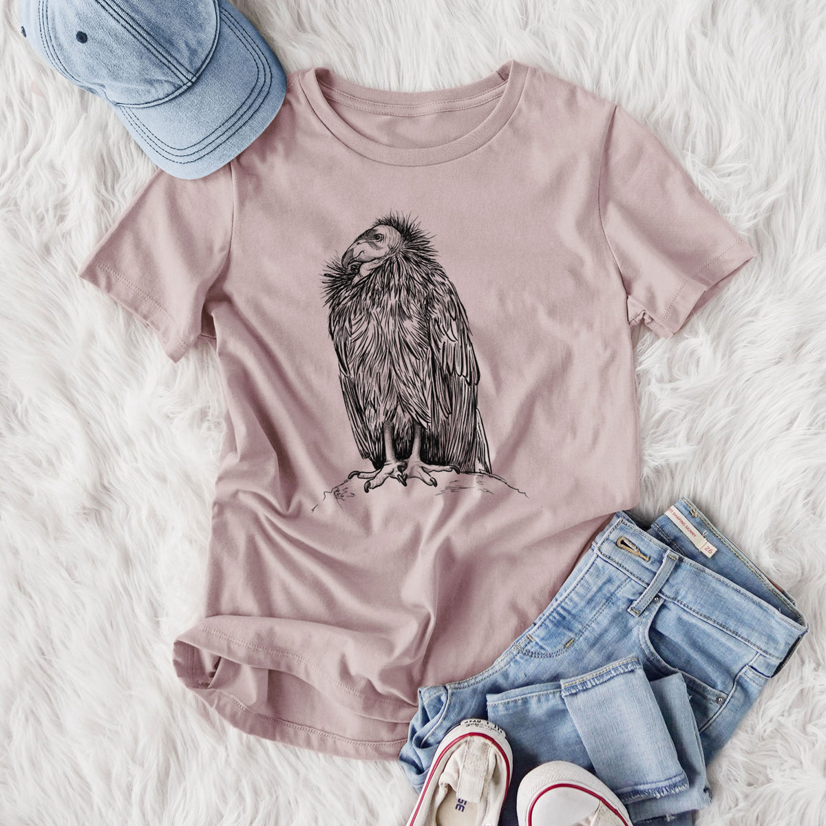 Women's relaxed fit cotton t-shirt printed with a detailed black ink illustration of a California condor perched with folded wings, styled flat on a white faux fur rug with jeans.