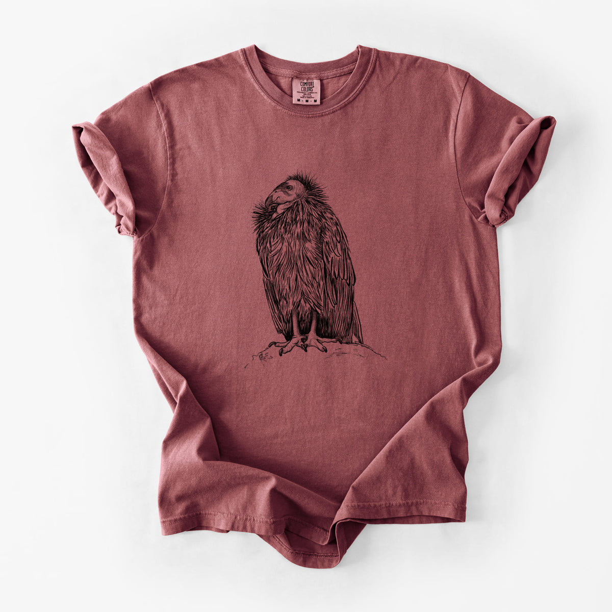 Brick red Comfort Colors t-shirt laid flat, printed with a detailed black ink illustration of a California condor perched with folded wings.