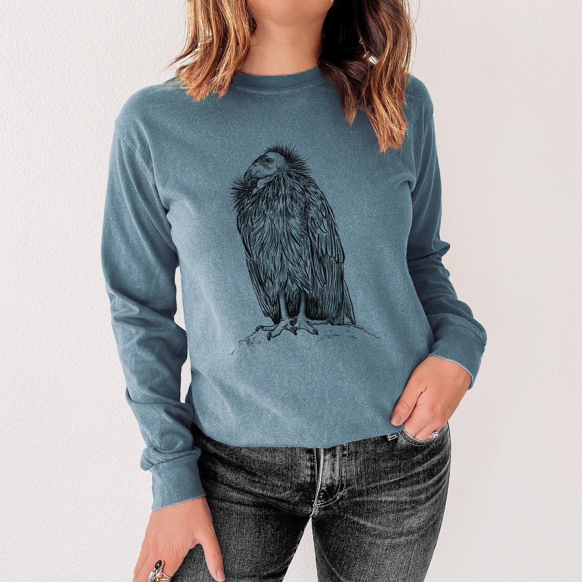 Steel blue Comfort Colors long sleeve shirt printed with a detailed black ink illustration of a California condor perched with folded wings, shown in a lifestyle photo.