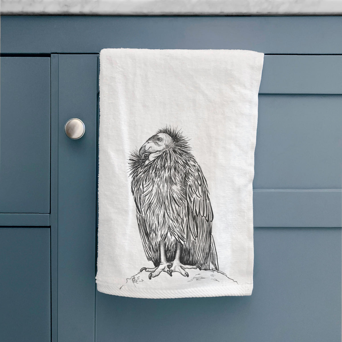 White hand towel printed with a detailed black ink illustration of a California condor perched with folded wings, hanging on a cabinet door.