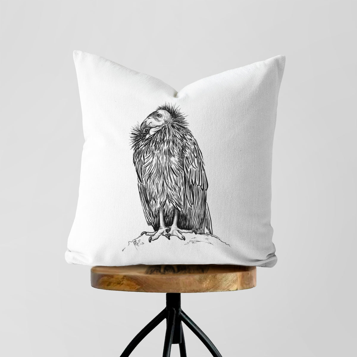 White pillow cover printed with a detailed black ink illustration of a California condor perched with folded wings, on a wooden stool.