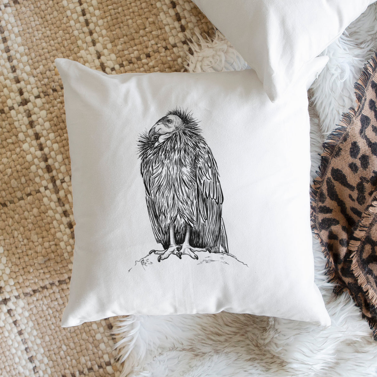 White pillow cover printed with a detailed black ink illustration of a California condor perched with folded wings, on a woven chair.