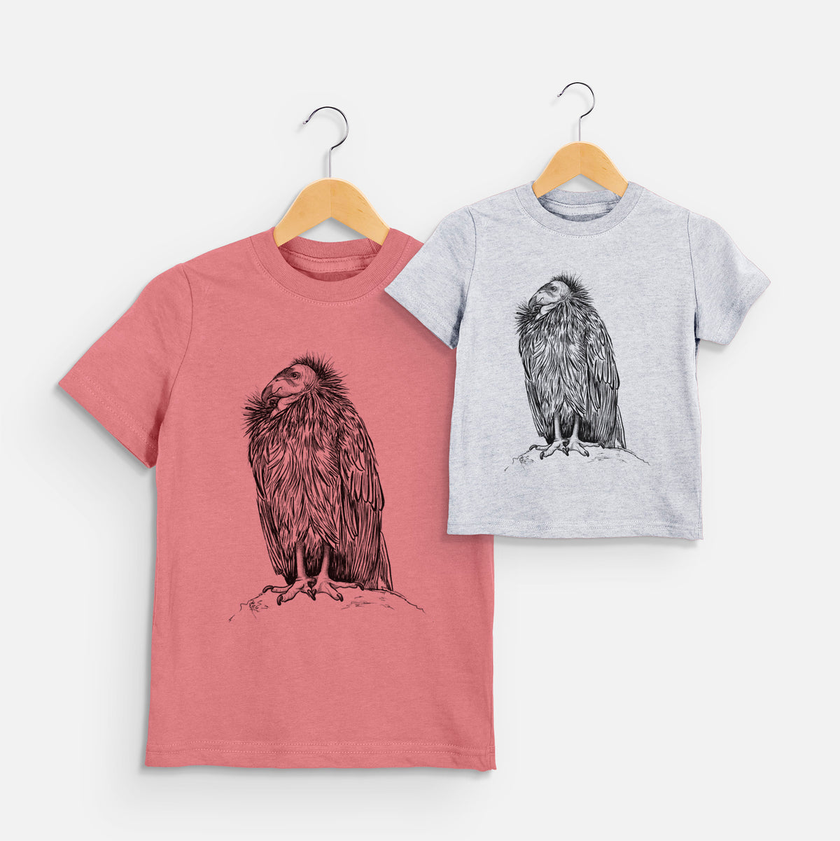 Two youth t-shirts in different colors on hangers, printed with a detailed black ink illustration of a California condor perched with folded wings.