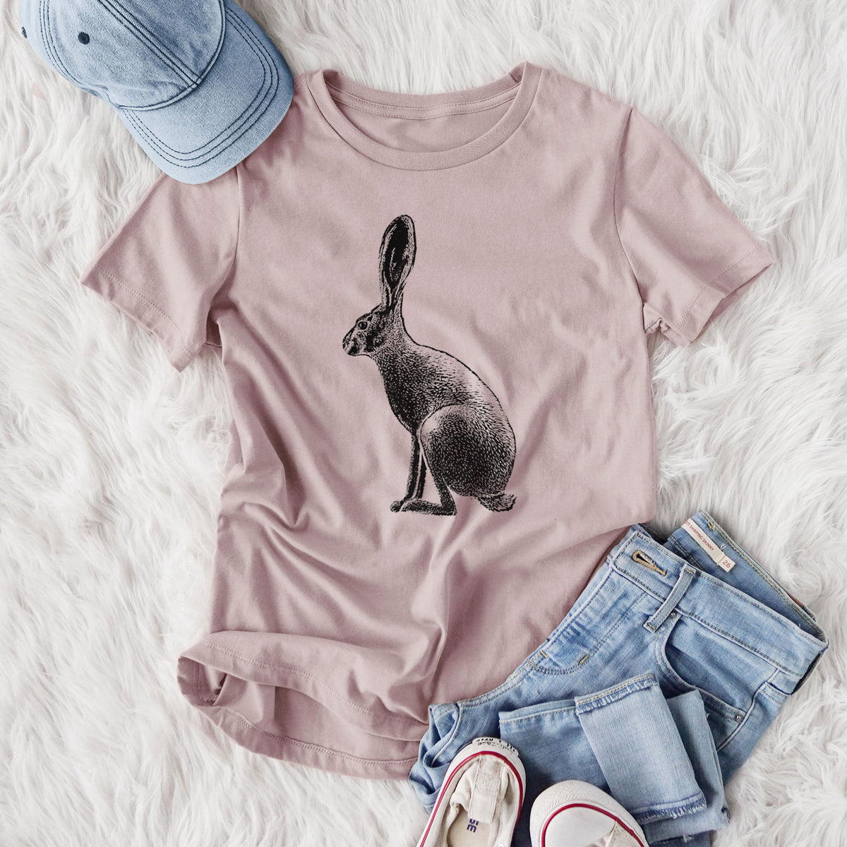 Women's relaxed fit cotton t-shirt printed with a detailed black ink illustration of a black-tailed jackrabbit sitting in profile with tall ears, styled flat on a white faux fur rug with jeans.