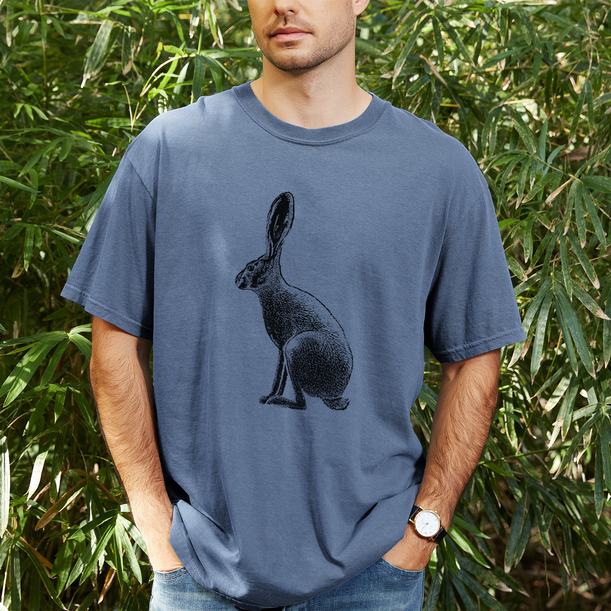 Man wearing a Comfort Colors t-shirt printed with a detailed black ink illustration of a black-tailed jackrabbit sitting in profile with tall ears, outdoors.