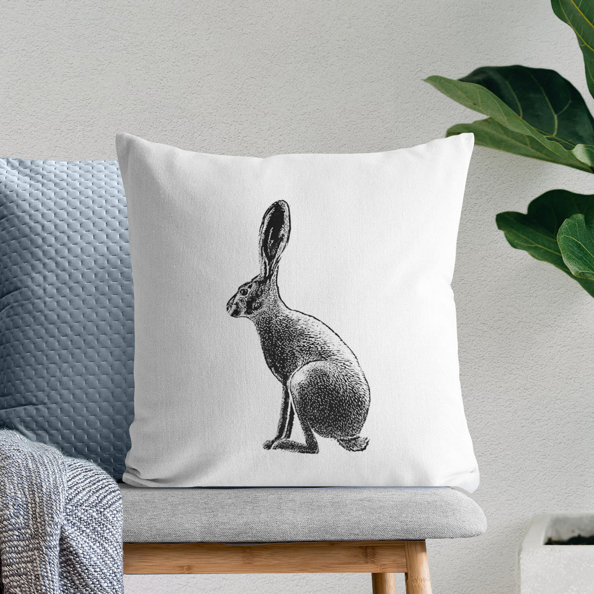 White pillow cover printed with a detailed black ink illustration of a black-tailed jackrabbit sitting in profile with tall ears, on a bench beside plants.