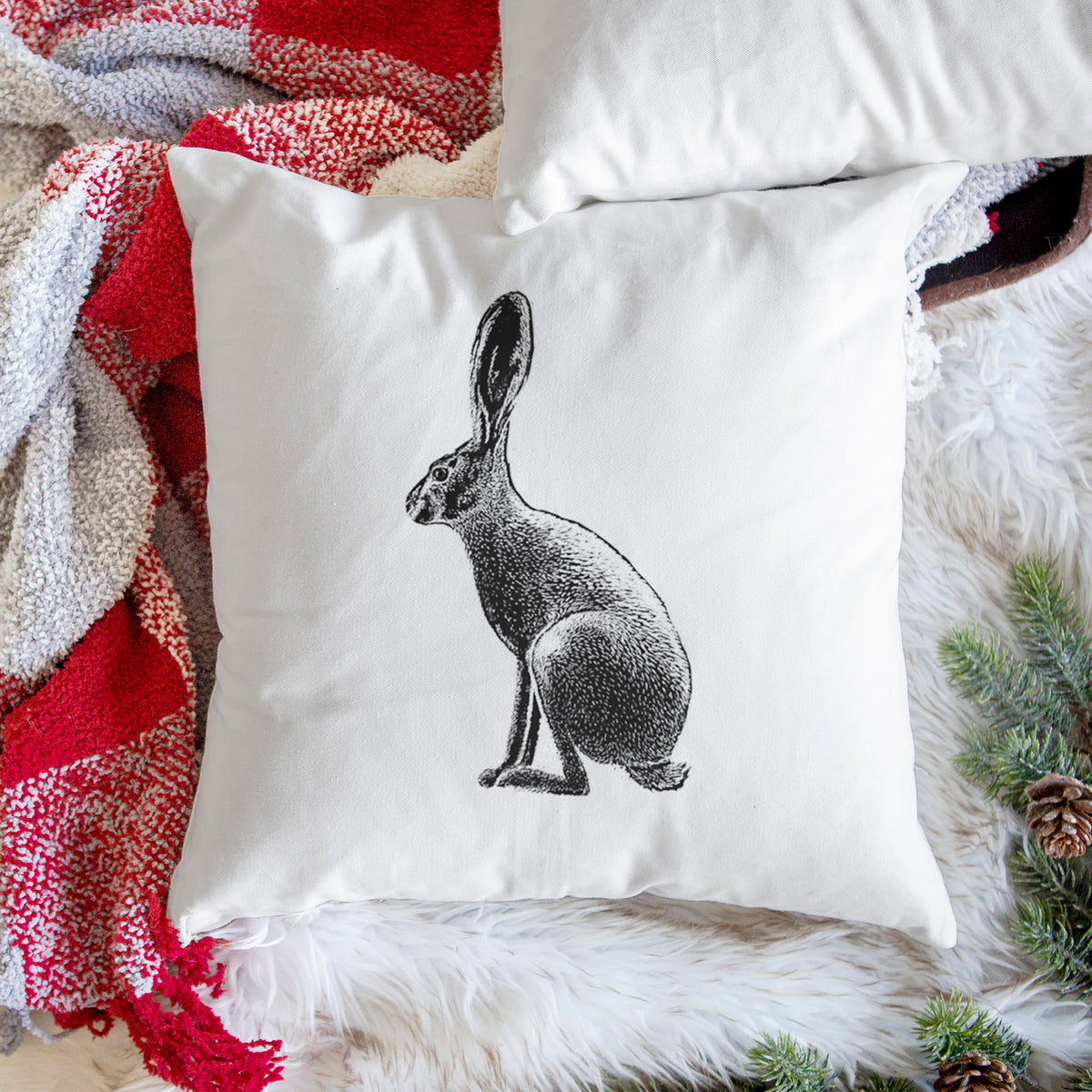 White pillow cover printed with a detailed black ink illustration of a black-tailed jackrabbit sitting in profile with tall ears, on a woven chair.