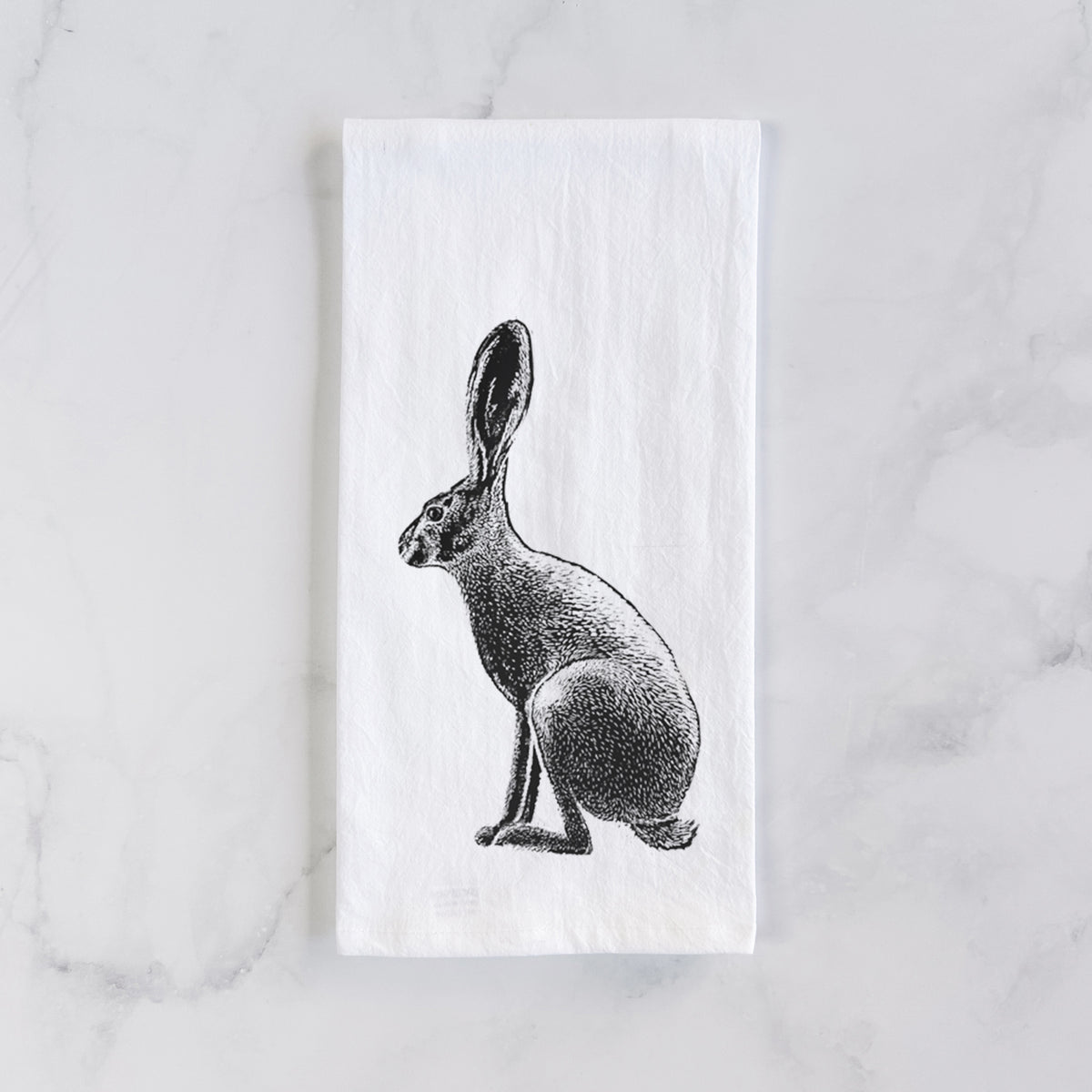 White cotton tea towel laid flat on marble, printed with a detailed black ink illustration of a black-tailed jackrabbit sitting in profile with tall ears.
