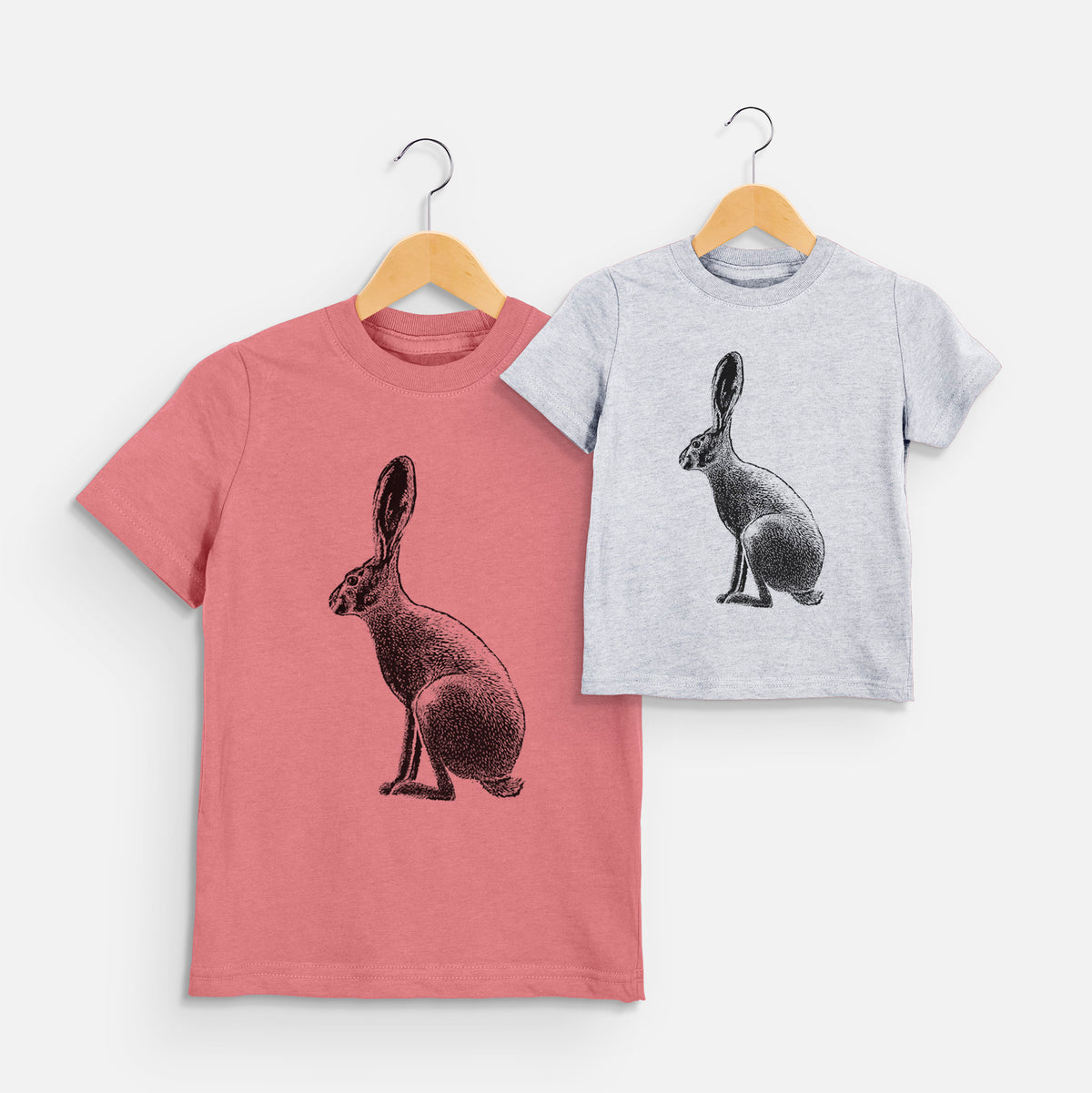 Two youth t-shirts in different colors on hangers, printed with a detailed black ink illustration of a black-tailed jackrabbit sitting in profile with tall ears.