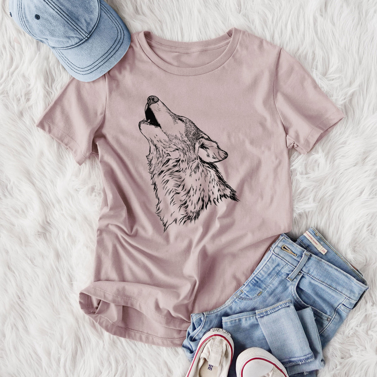 Women's relaxed fit cotton t-shirt printed with a detailed black ink illustration of a grey wolf's head and shoulders, howling upward, styled flat on a white faux fur rug with jeans.