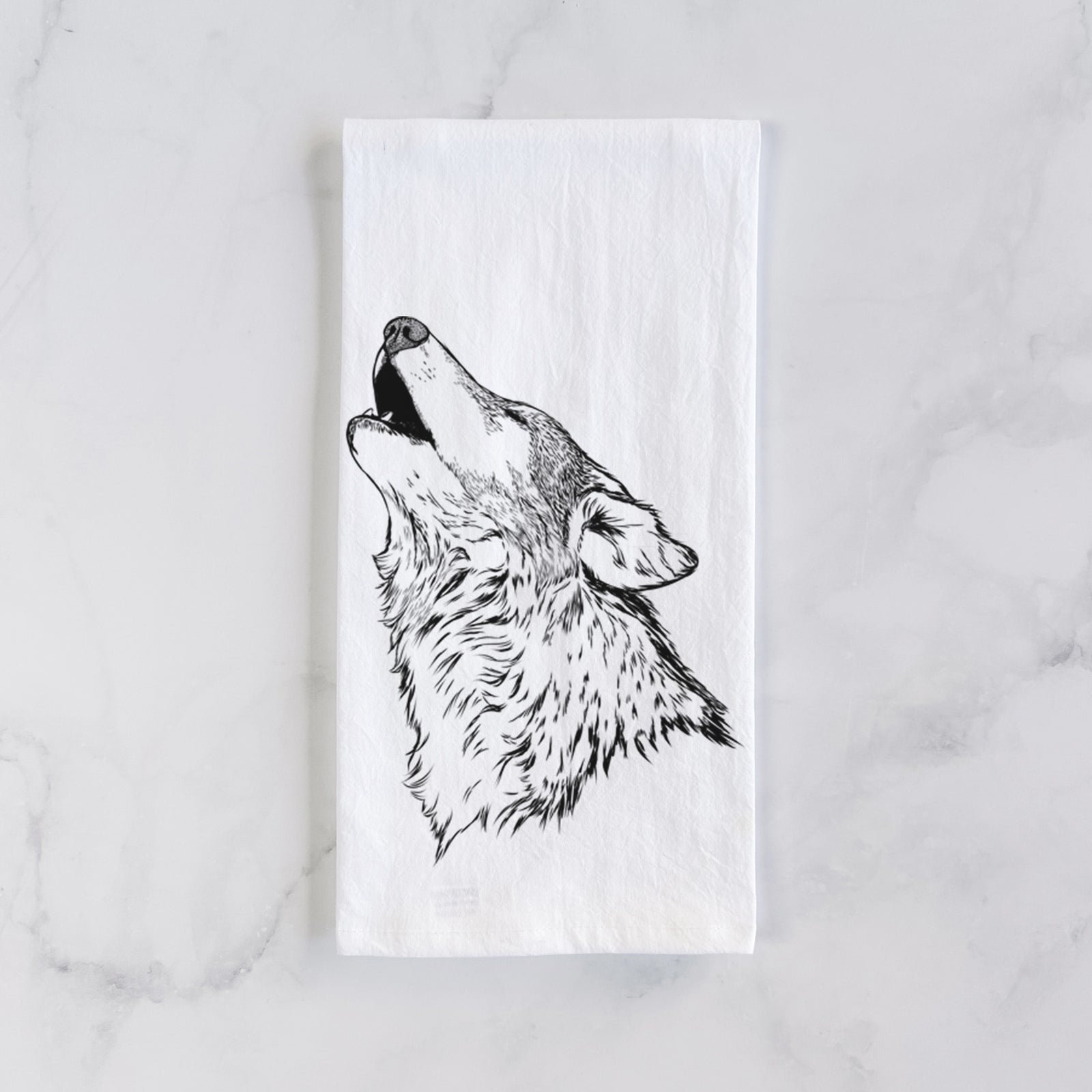 White cotton tea towel printed with a detailed black ink illustration of a grey wolf's head and shoulders, howling upward, on a marble counter beside a round wooden cutting board and greenery.