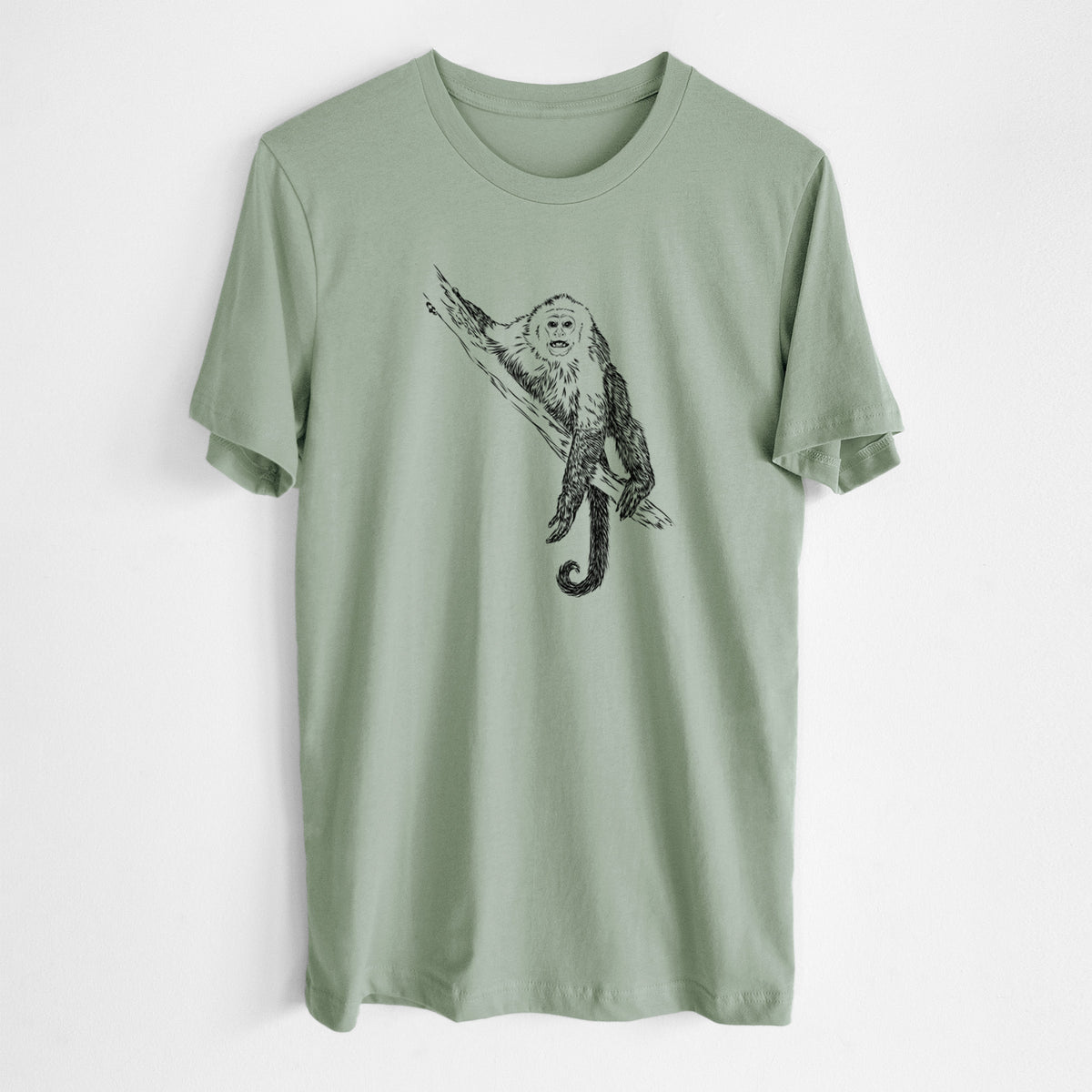 Sage green lightweight cotton t-shirt laid flat, printed with a detailed black ink illustration of a capuchin monkey climbing a branch.