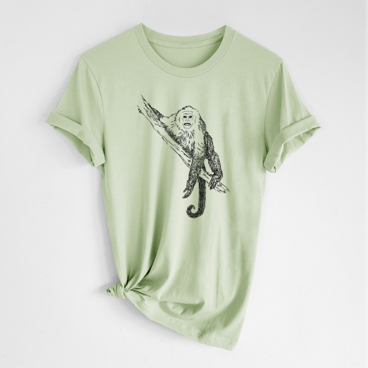 Spring green lightweight cotton t-shirt laid flat with the sleeves rolled, printed with a detailed black ink illustration of a capuchin monkey climbing a branch.
