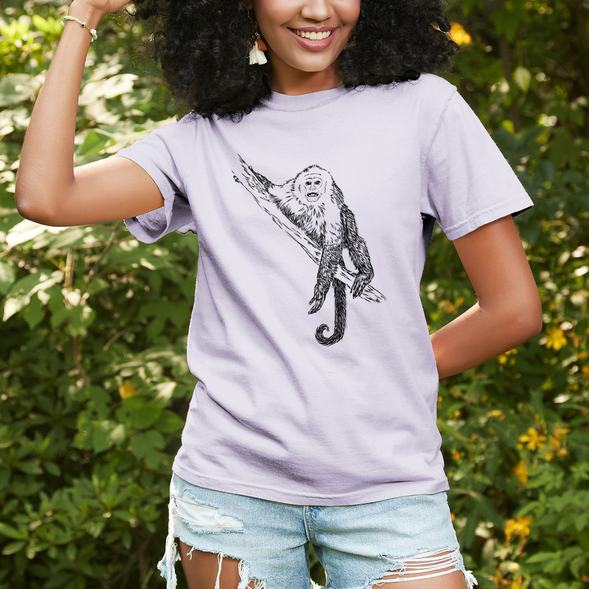 Woman wearing a Comfort Colors t-shirt printed with a detailed black ink illustration of a capuchin monkey climbing a branch, outdoors.