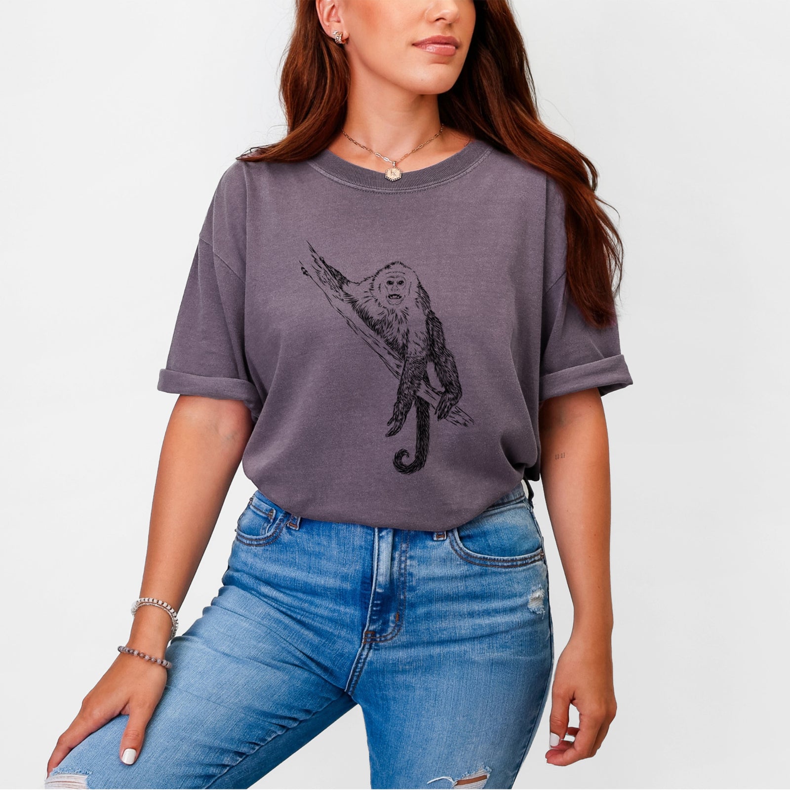 Blue jean Comfort Colors t-shirt laid flat, printed with a detailed black ink illustration of a capuchin monkey climbing a branch.