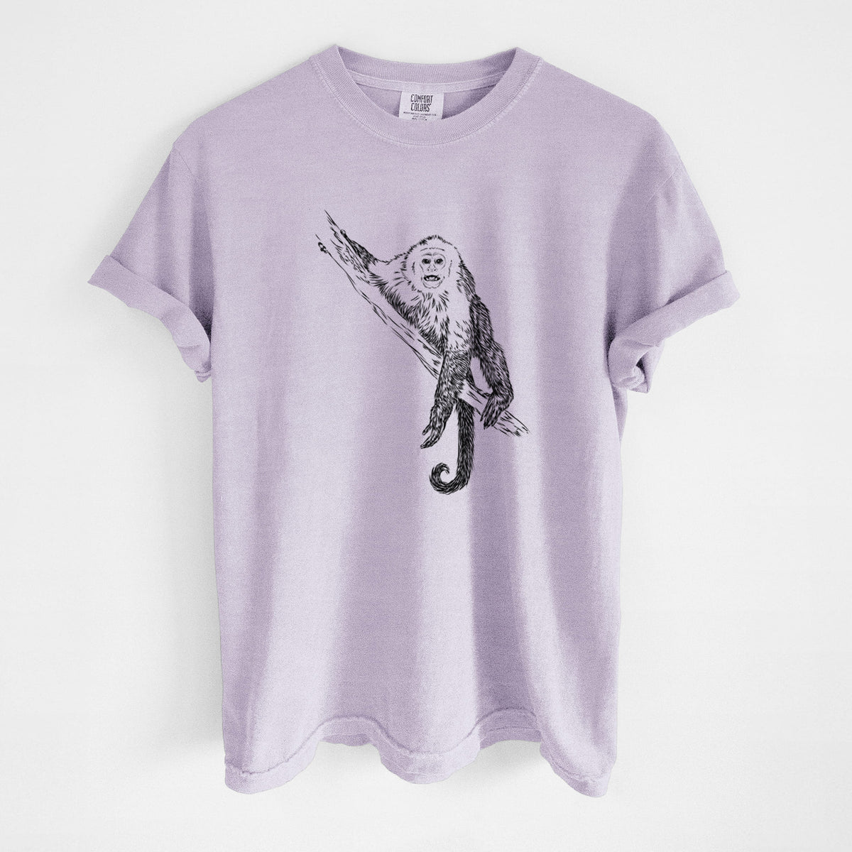 Orchid purple Comfort Colors t-shirt laid flat, printed with a detailed black ink illustration of a capuchin monkey climbing a branch.