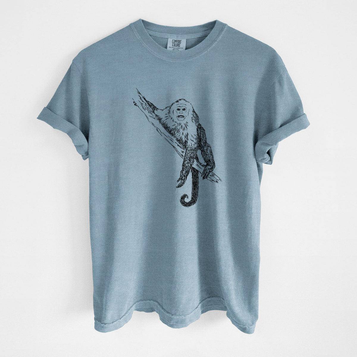 Steel blue Comfort Colors t-shirt laid flat, printed with a detailed black ink illustration of a capuchin monkey climbing a branch.