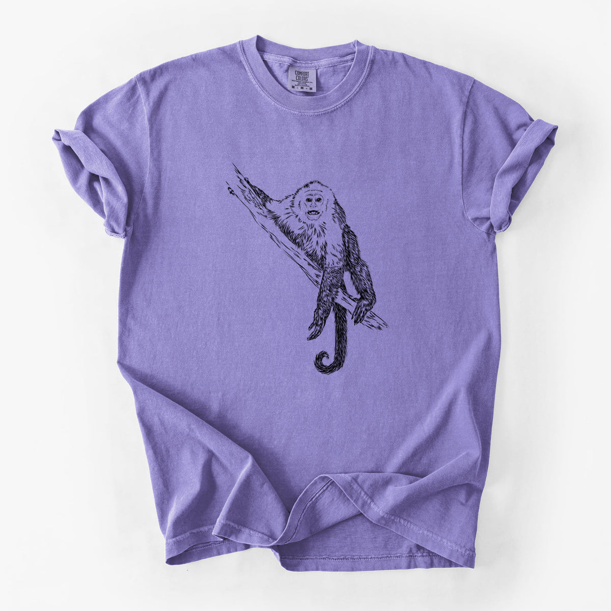 Violet purple Comfort Colors t-shirt laid flat, printed with a detailed black ink illustration of a capuchin monkey climbing a branch.