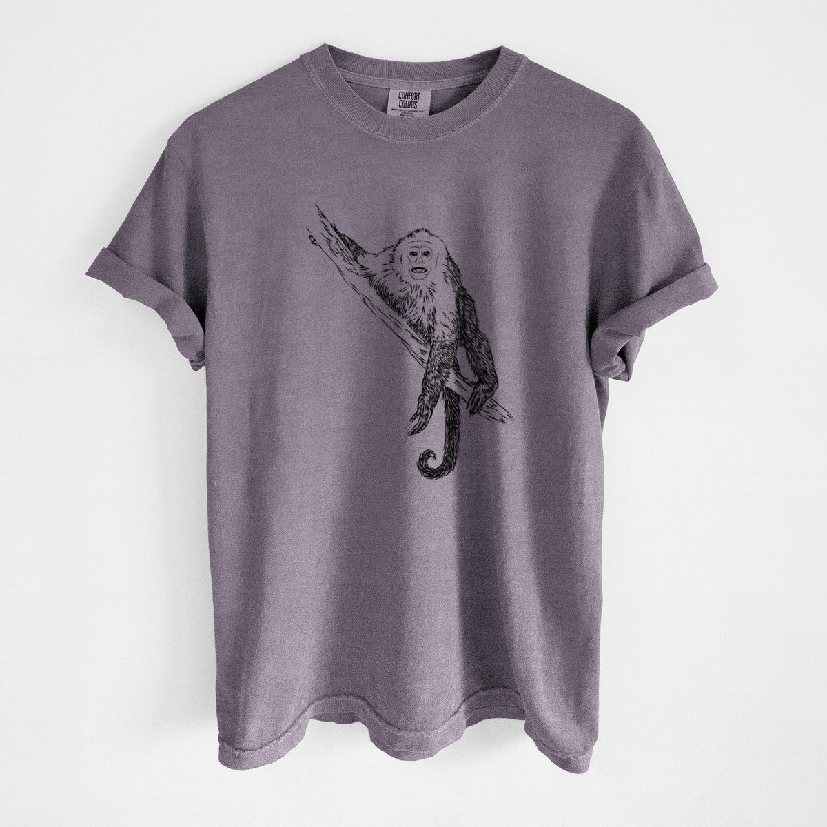 Wine red Comfort Colors t-shirt laid flat, printed with a detailed black ink illustration of a capuchin monkey climbing a branch.
