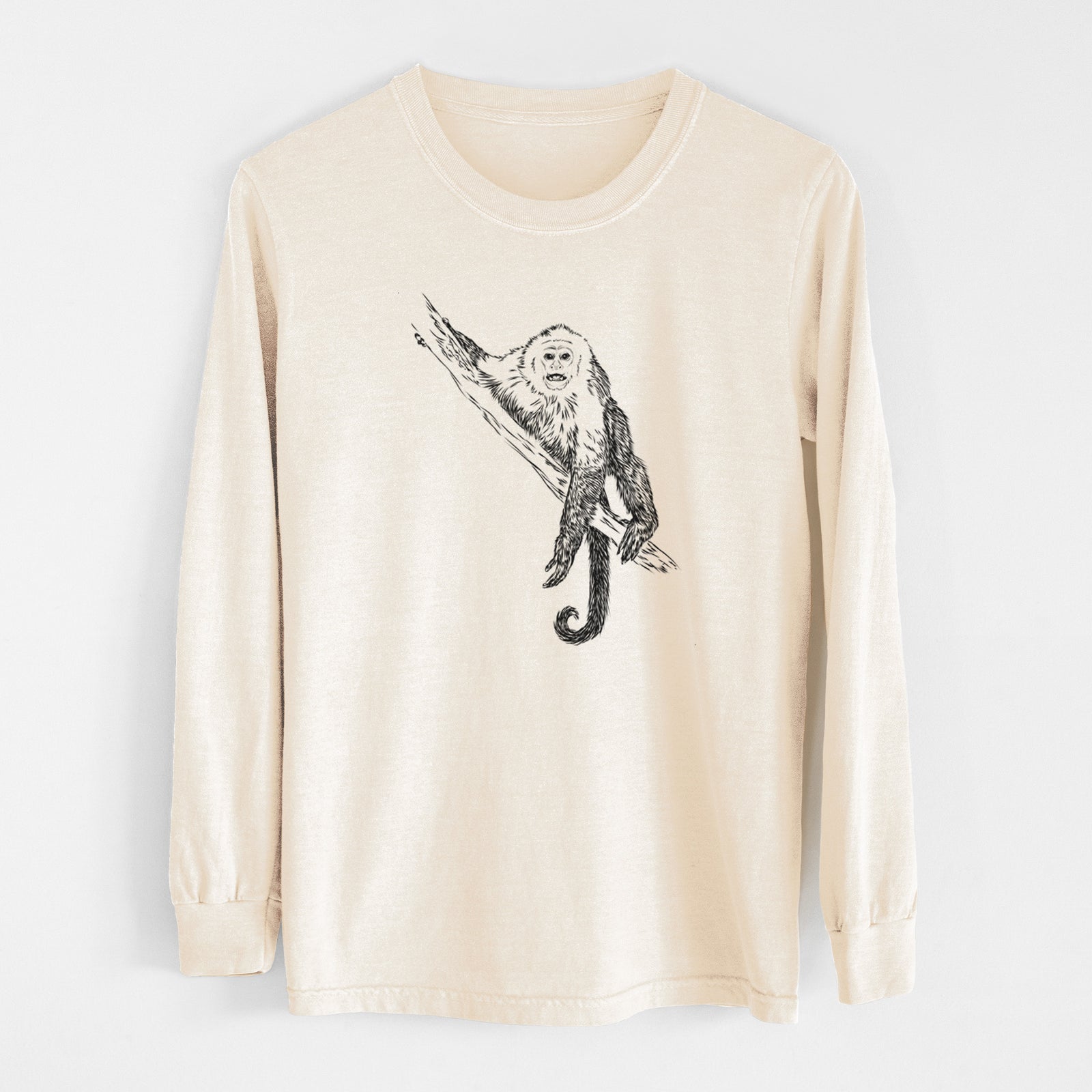 Ivory Comfort Colors long sleeve shirt laid flat, printed with a detailed black ink illustration of a capuchin monkey climbing a branch.