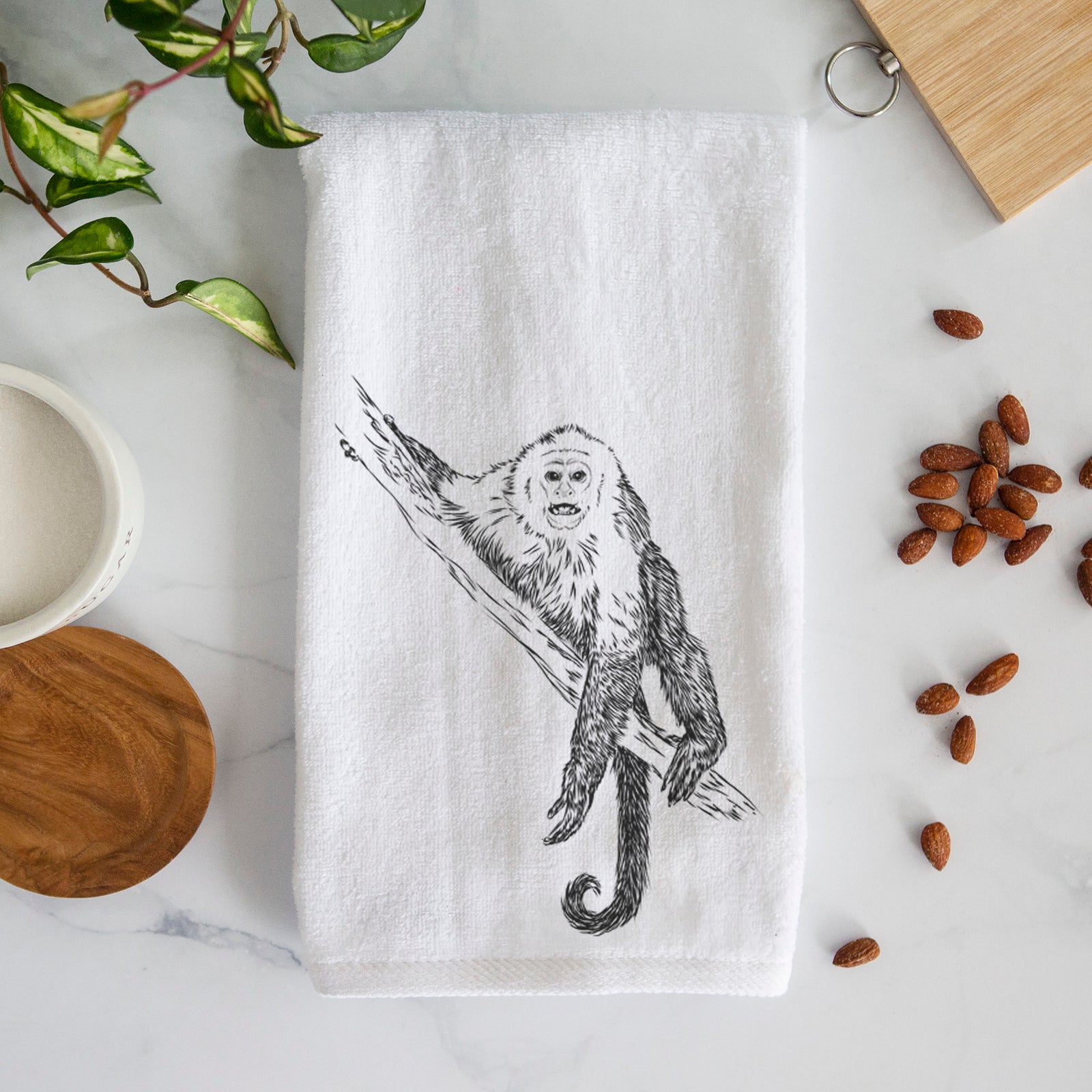 White hand towel printed with a detailed black ink illustration of a capuchin monkey climbing a branch.