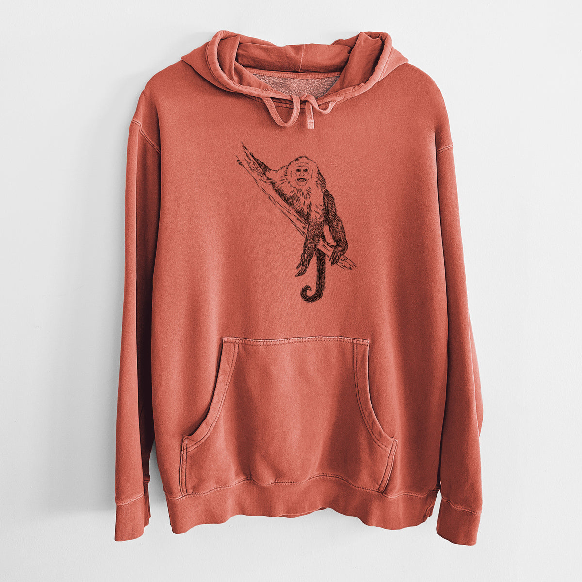 Amber orange pigment dyed hoodie laid flat, printed with a detailed black ink illustration of a capuchin monkey climbing a branch.