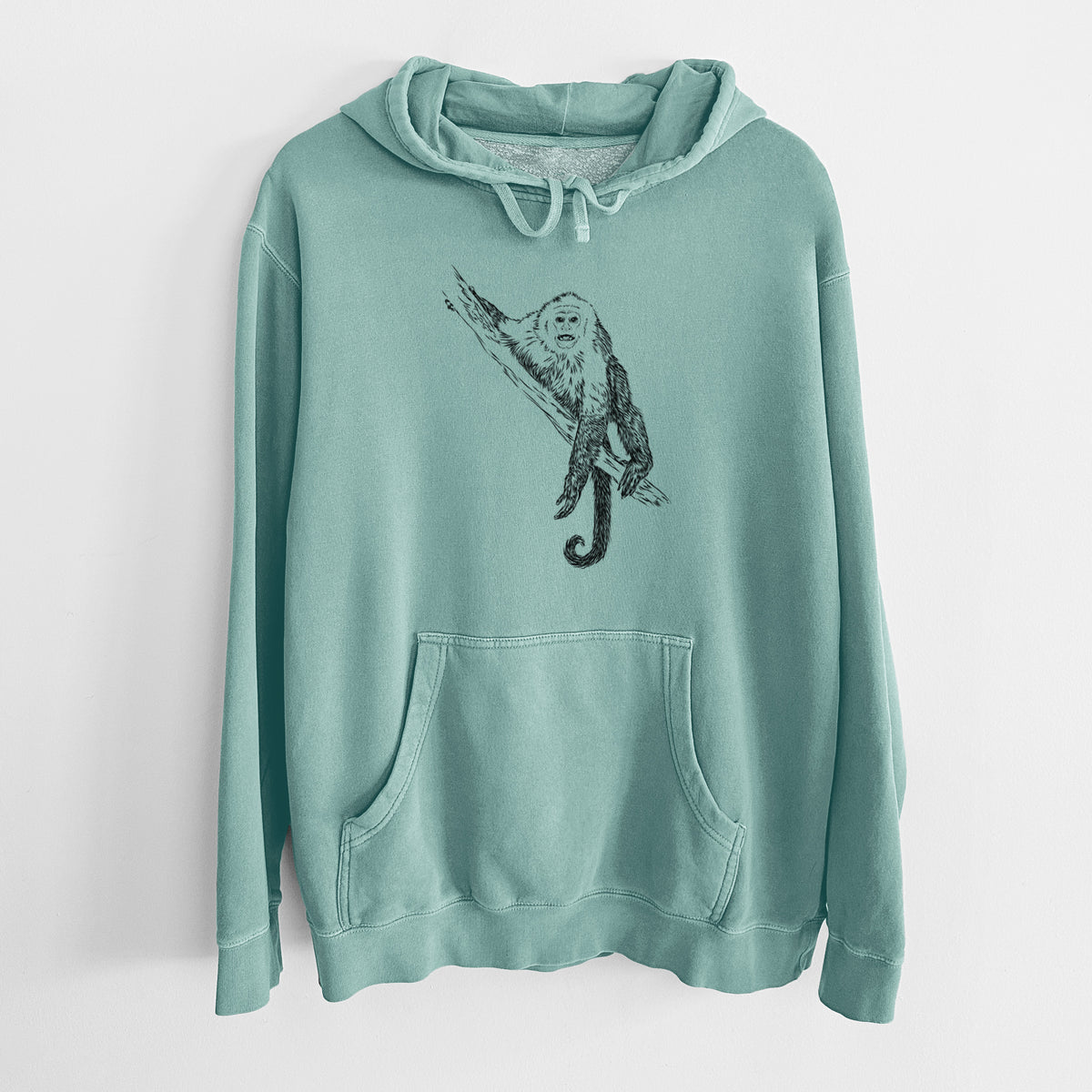 Mint green pigment dyed hoodie laid flat, printed with a detailed black ink illustration of a capuchin monkey climbing a branch.