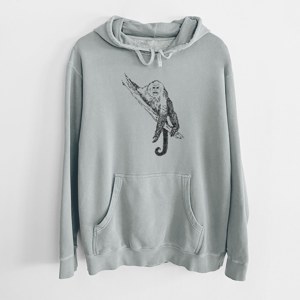 Sage green pigment dyed hoodie laid flat, printed with a detailed black ink illustration of a capuchin monkey climbing a branch.