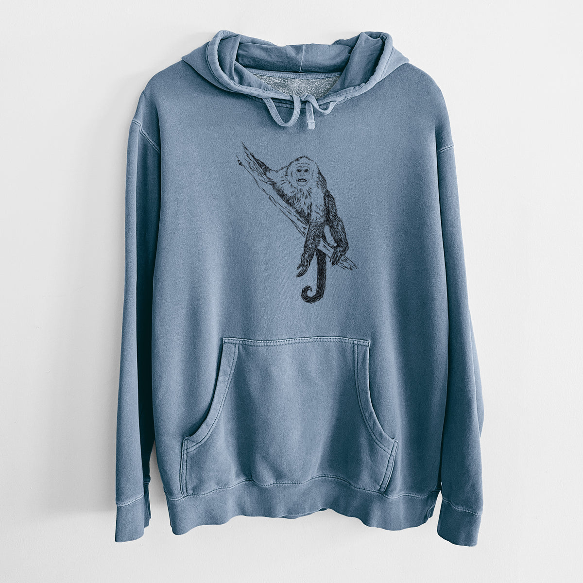 Slate blue pigment dyed hoodie laid flat, printed with a detailed black ink illustration of a capuchin monkey climbing a branch.