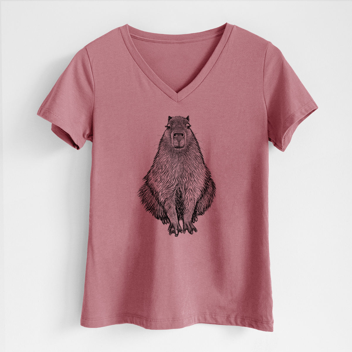 Mauve pink women's relaxed fit cotton V-neck t-shirt laid flat, printed with a detailed black ink illustration of a capybara sitting and facing forward.