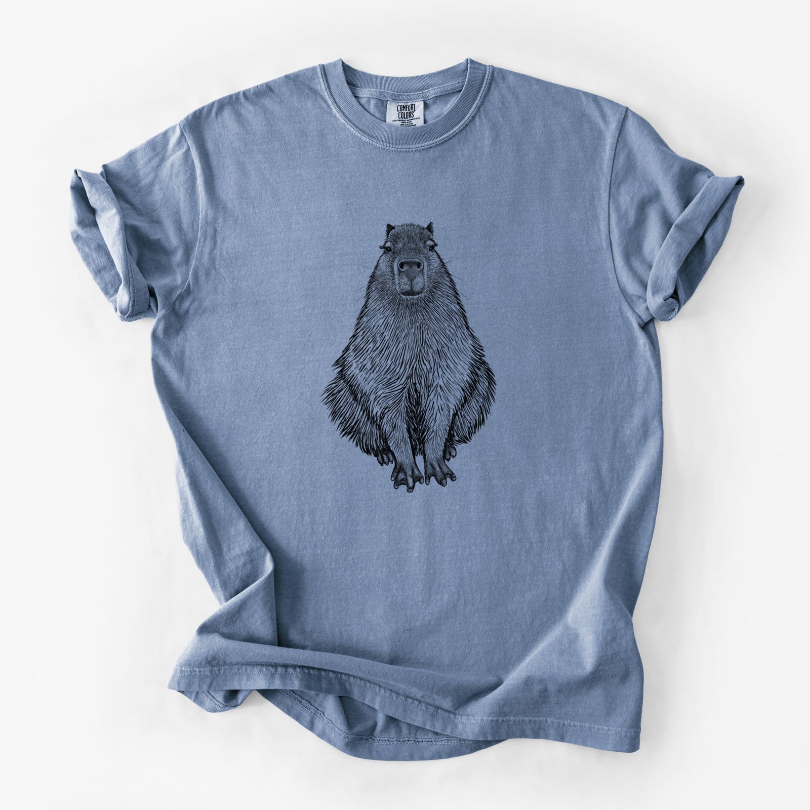 Blue jean Comfort Colors t-shirt laid flat, printed with a detailed black ink illustration of a capybara sitting and facing forward.