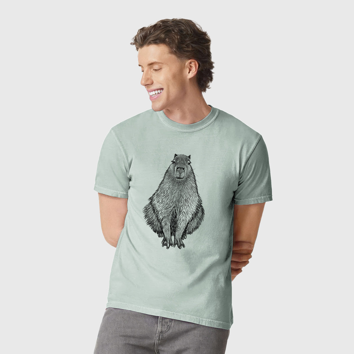 Man wearing a Comfort Colors t-shirt printed with a detailed black ink illustration of a capybara sitting and facing forward.