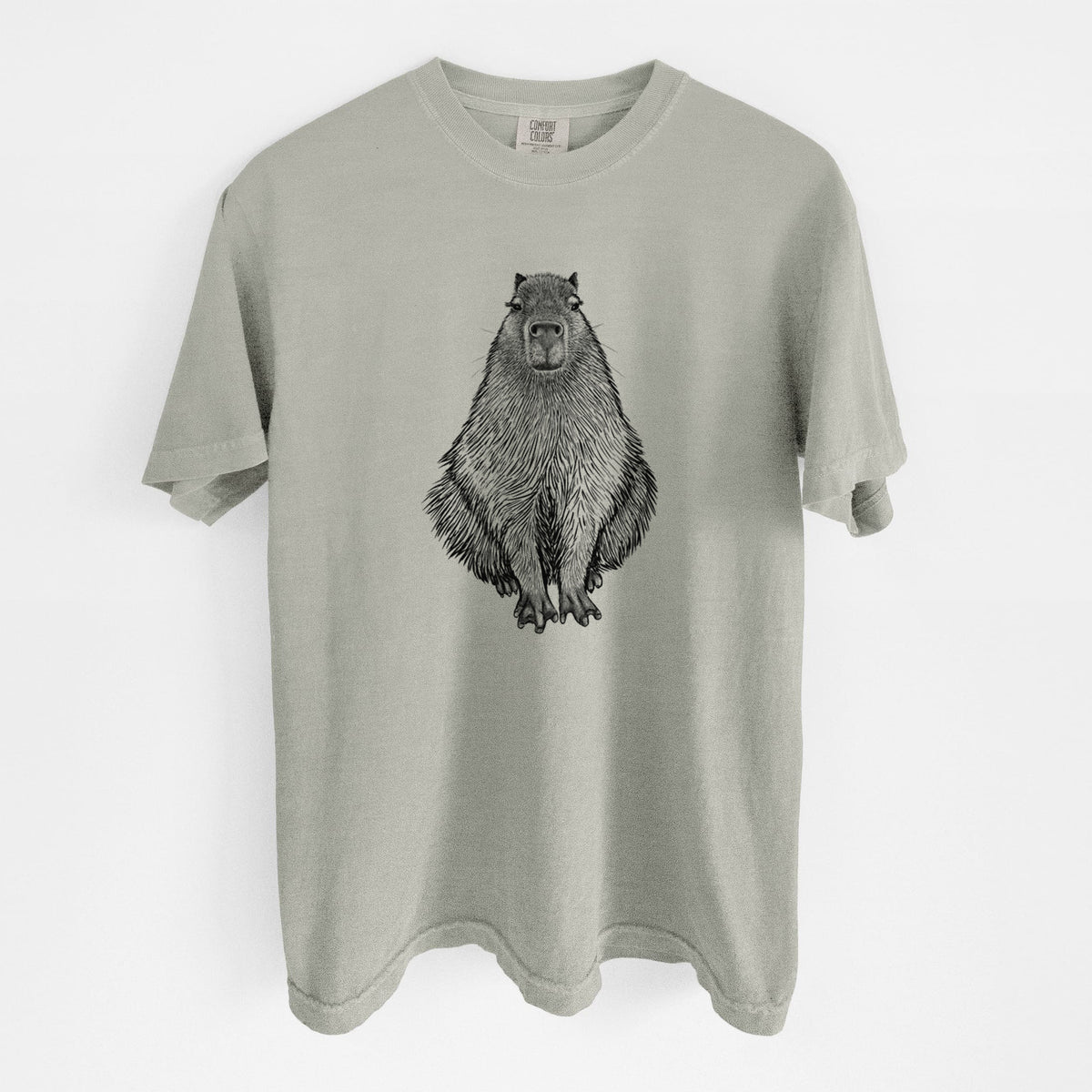 Sandstone beige Comfort Colors t-shirt laid flat, printed with a detailed black ink illustration of a capybara sitting and facing forward.