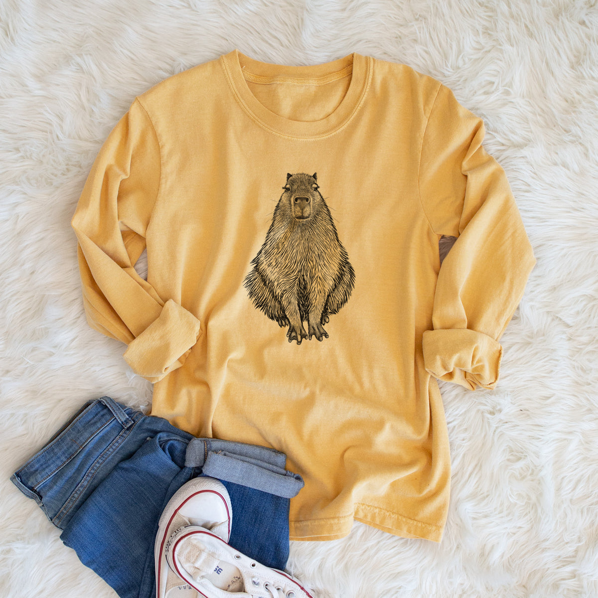 Golden wheat yellow Comfort Colors long sleeve shirt printed with a detailed black ink illustration of a capybara sitting and facing forward, shown in a lifestyle photo.