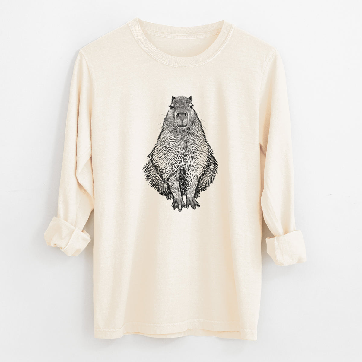 Ivory Comfort Colors long sleeve shirt laid flat with the cuffs rolled, printed with a detailed black ink illustration of a capybara sitting and facing forward.