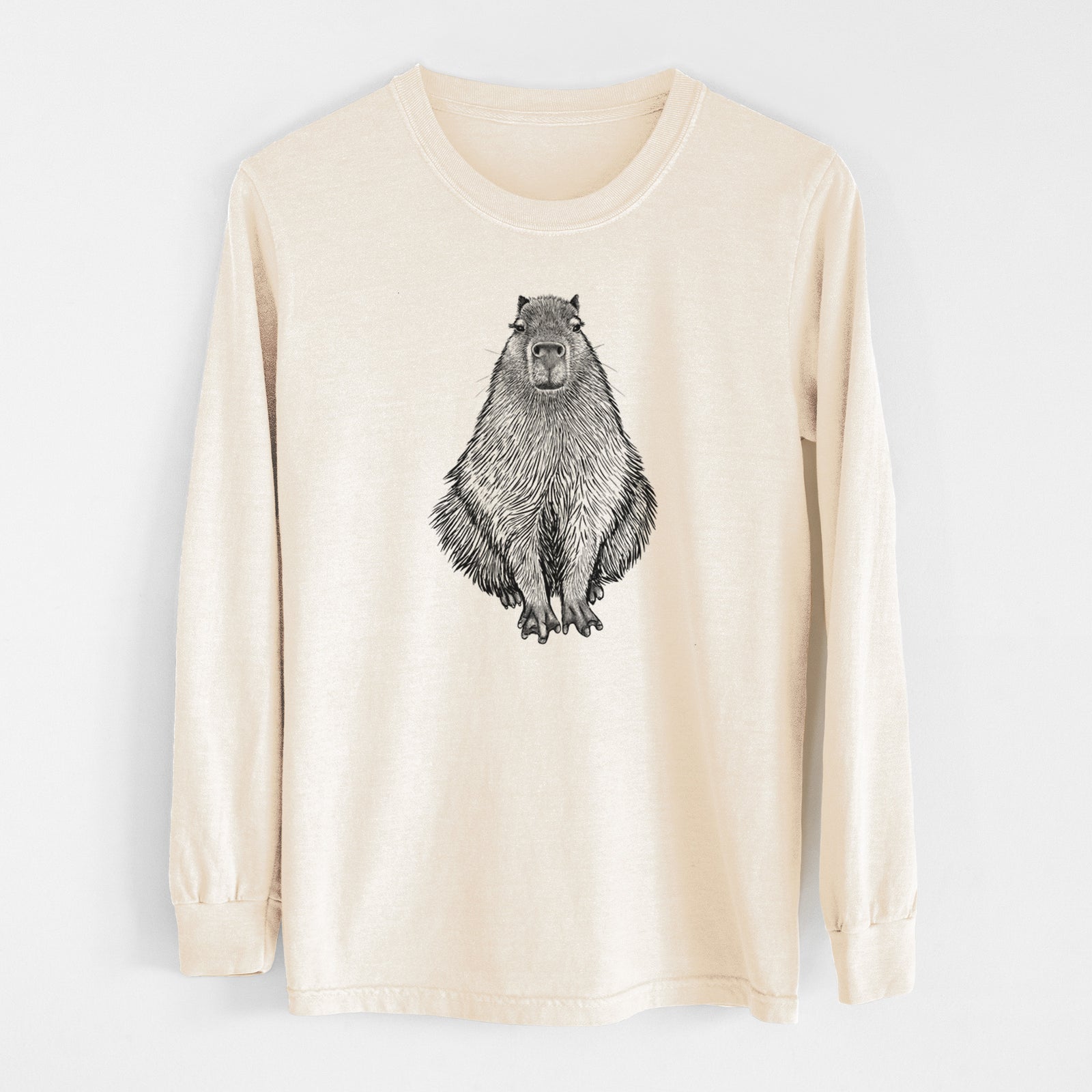 Ivory Comfort Colors long sleeve shirt laid flat, printed with a detailed black ink illustration of a capybara sitting and facing forward.