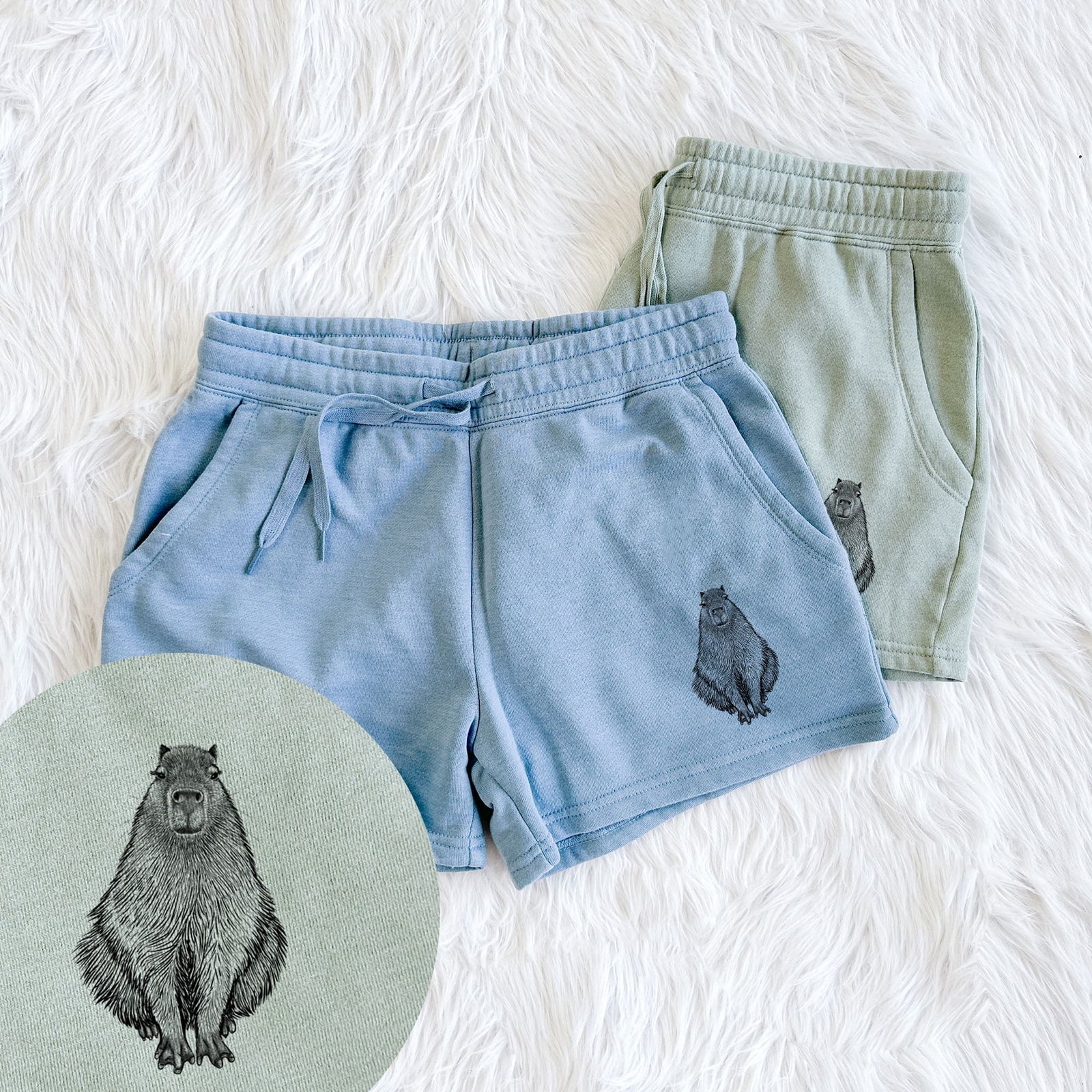 Two pairs of Cali Wave shorts in different colors printed with a detailed black ink illustration of a capybara sitting and facing forward, with a close-up of the print.