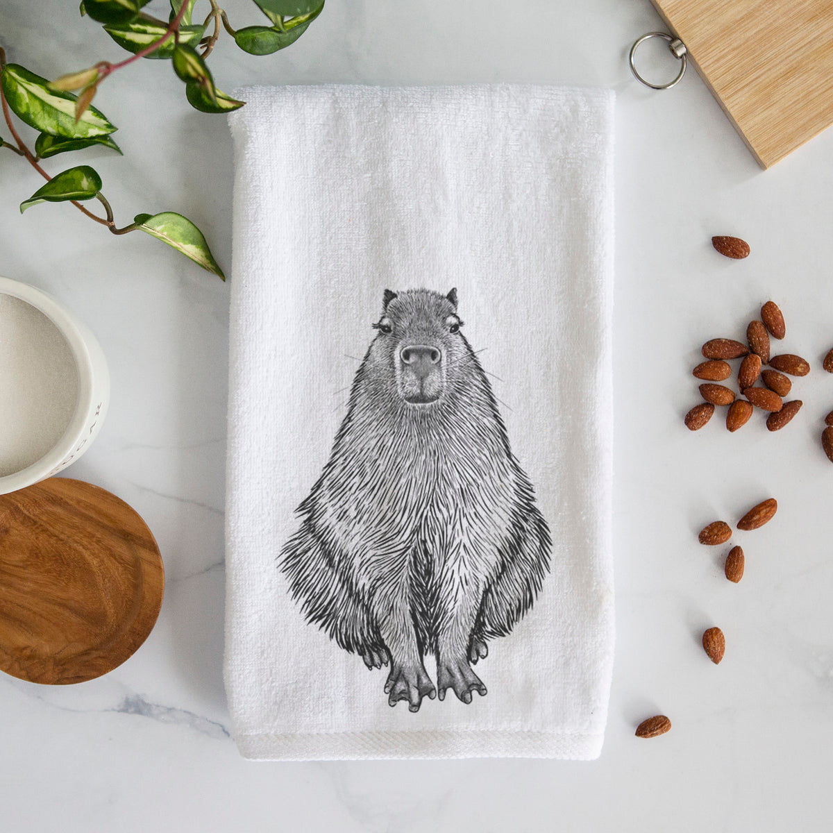 White hand towel printed with a detailed black ink illustration of a capybara sitting and facing forward.