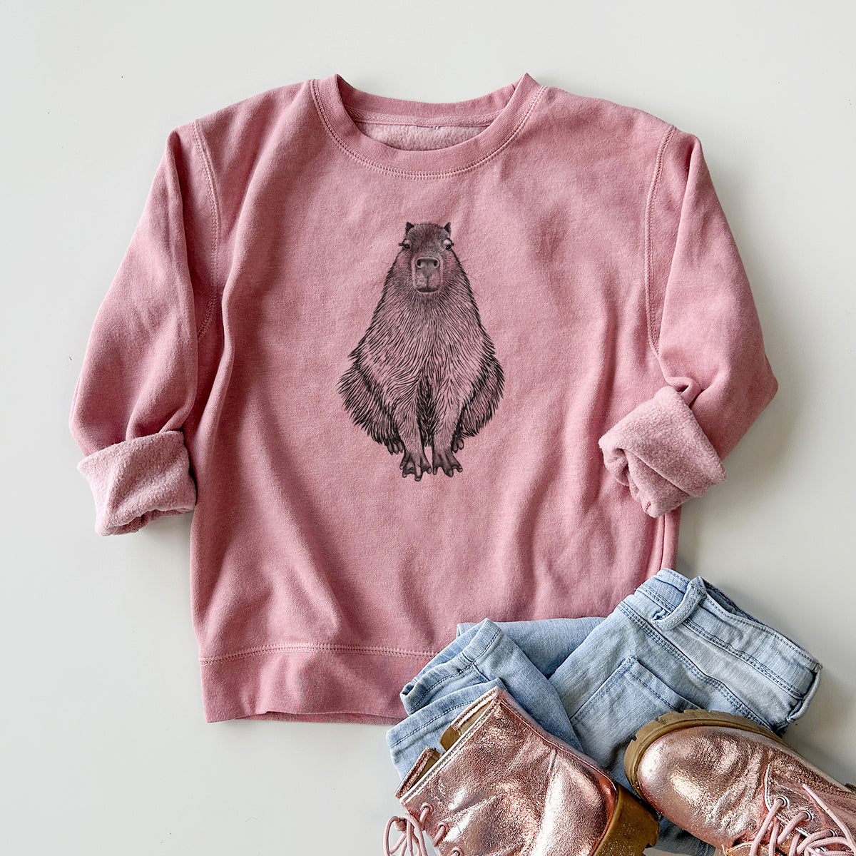 Youth crewneck sweatshirt printed with a detailed black ink illustration of a capybara sitting and facing forward, styled flat with jeans and boots.