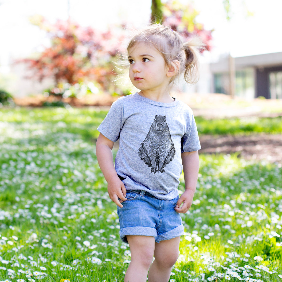 Toddler girl walking outdoors wearing a t-shirt printed with a detailed black ink illustration of a capybara sitting and facing forward.