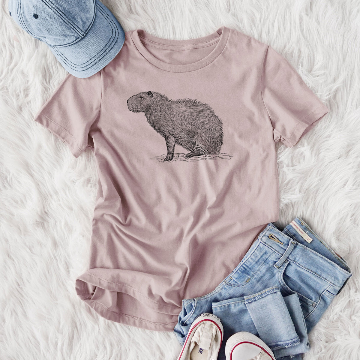 Women's relaxed fit cotton t-shirt printed with a detailed black ink illustration of a capybara standing in profile, styled flat on a white faux fur rug with jeans.