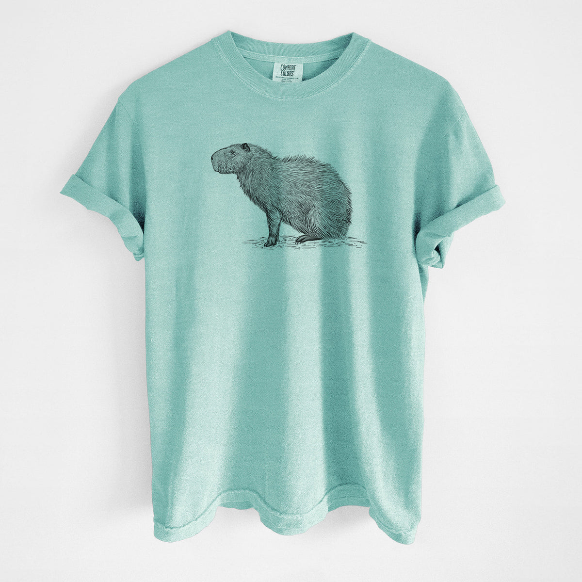 Chalky mint Comfort Colors t-shirt laid flat, printed with a detailed black ink illustration of a capybara standing in profile.