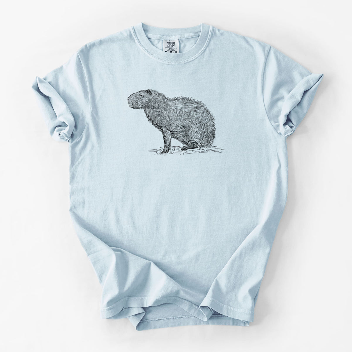 Chambray blue Comfort Colors t-shirt laid flat, printed with a detailed black ink illustration of a capybara standing in profile.