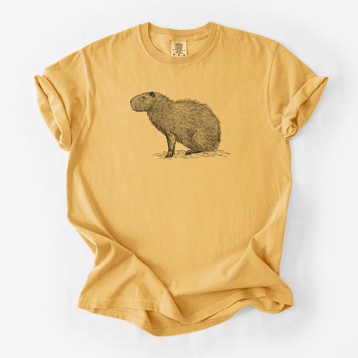Golden wheat yellow Comfort Colors t-shirt laid flat, printed with a detailed black ink illustration of a capybara standing in profile.