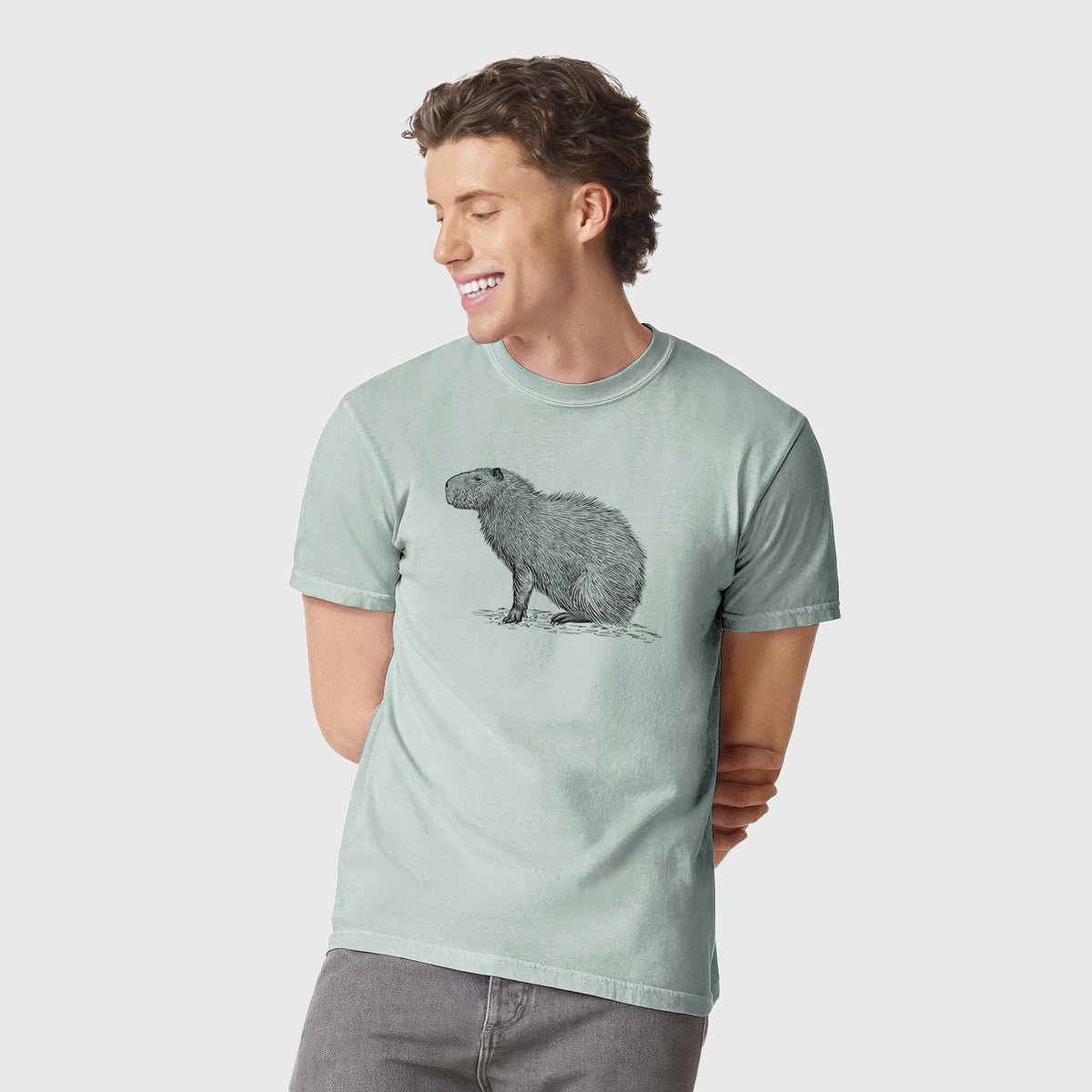 Man wearing a Comfort Colors t-shirt printed with a detailed black ink illustration of a capybara standing in profile.