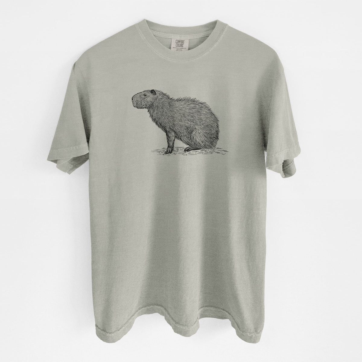 Sandstone beige Comfort Colors t-shirt laid flat, printed with a detailed black ink illustration of a capybara standing in profile.