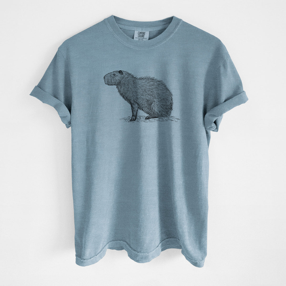Steel blue Comfort Colors t-shirt laid flat, printed with a detailed black ink illustration of a capybara standing in profile.